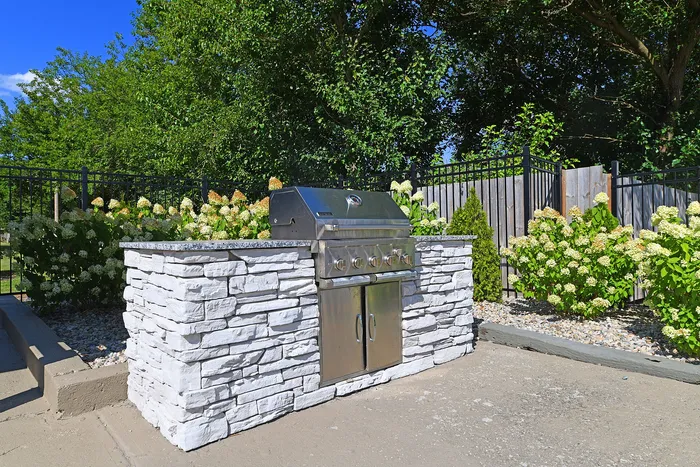 Chic outdoor barbecue setup with a sleek stainless steel grill and stylish stone counter, surrounded by lush greenery and vibrant flowers.