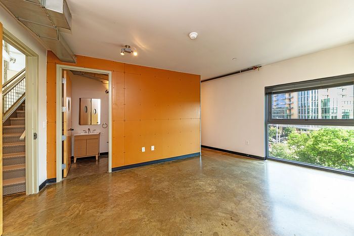 Bright, modern apartment with large windows, city views, and stylish industrial accents, featuring a sleek bathroom adjoining the spacious open area.