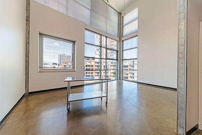 Bright and airy room with expansive floor-to-ceiling windows showcasing stunning city views, modern minimalist design, and polished concrete floors.