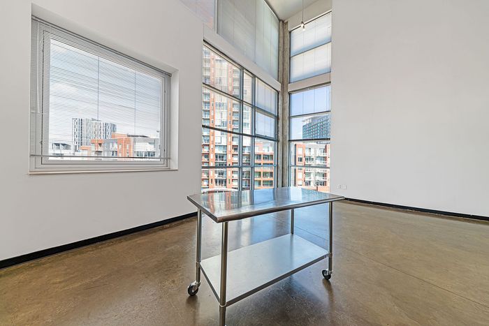 Bright and spacious apartment with large windows overlooking a modern cityscape, featuring sleek floors and a versatile metal table on wheels.