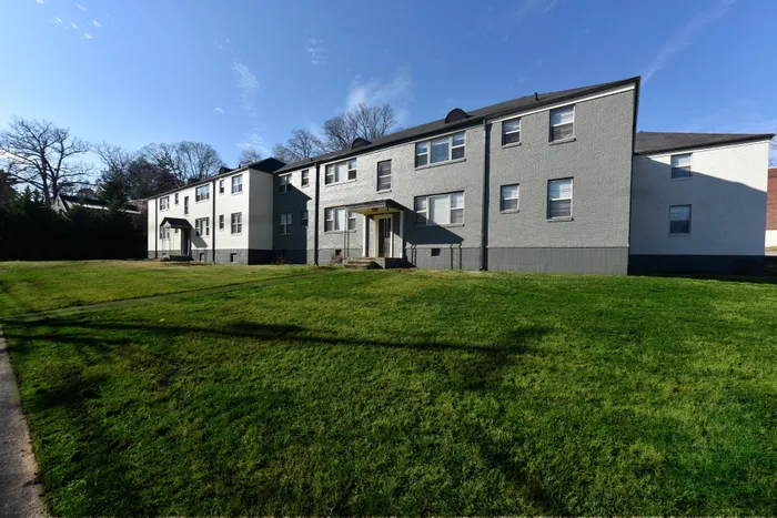 Charming apartment building with spacious green lawn and modern gray facade, basking in the morning sunlight.