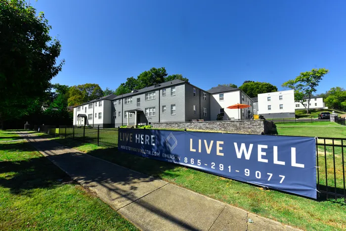 Inviting apartment complex with spacious green lawns and modern architecture, promoting prime living with the motto 'Live Here, Live Well'.