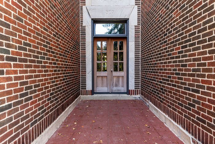 Charming entrance with elegant wooden double doors framed by classic red brick walls, adding a warm and inviting touch to the building.