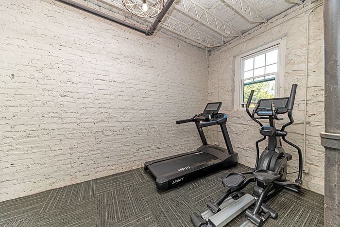 Chic apartment fitness room with a treadmill and elliptical, featuring exposed brick and cozy natural light.