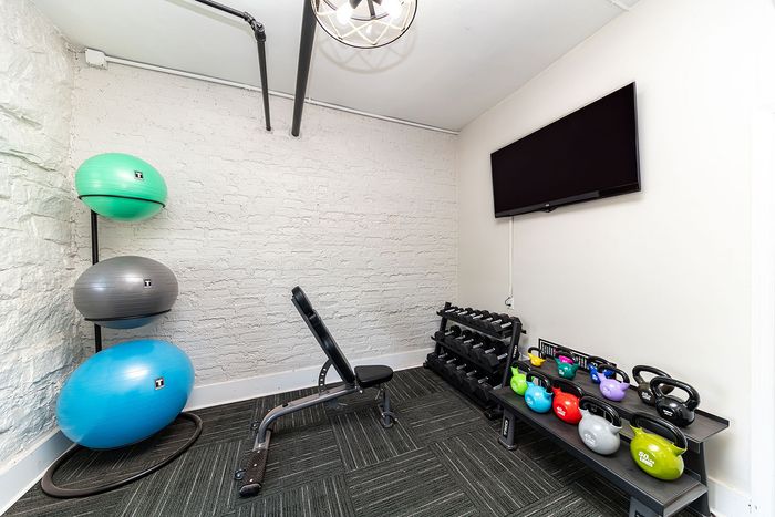 Modern home gym with a sleek bench, vibrant exercise balls, colorful kettlebells, and a rack of dumbbells, perfect for a private workout retreat.