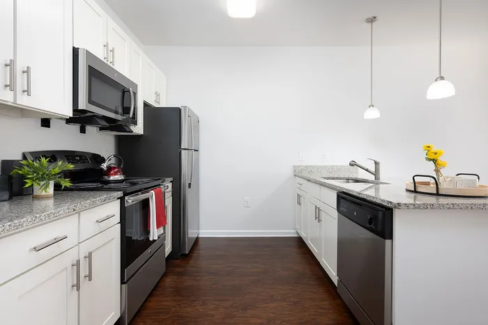 Modern kitchen with sleek stainless steel appliances, white cabinetry, and elegant granite countertops accented by pendant lighting.