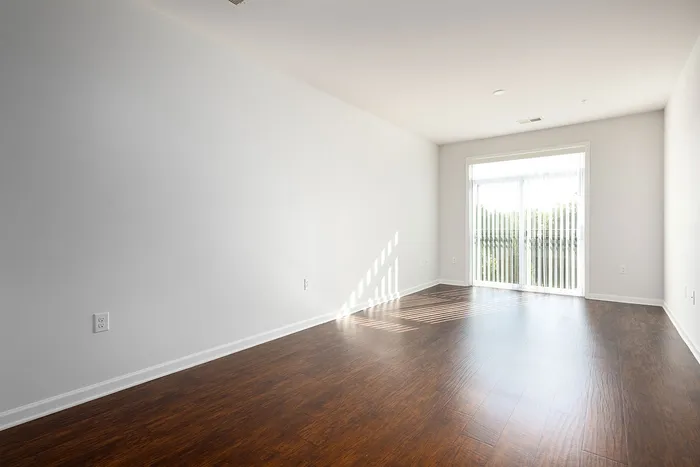 Bright and spacious room with elegant hardwood flooring, featuring large windows that invite natural light.