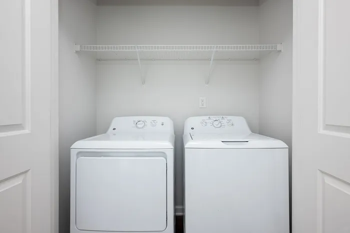 Modern laundry room featuring a sleek white washer and dryer with a convenient overhead shelving unit.