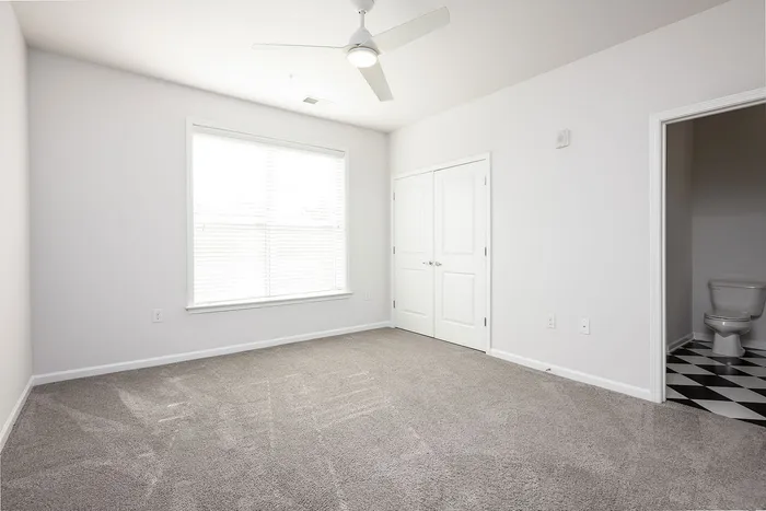 Bright and airy bedroom with plush carpet, large window, and stylish en-suite bathroom boasting chic flooring.