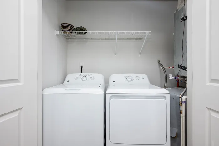 Modern laundry room with a sleek washer and dryer, complemented by a stylish overhead shelf for storage.