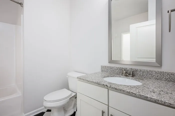 Modern bathroom featuring elegant granite countertop, sleek fixtures, and a pristine white aesthetic.