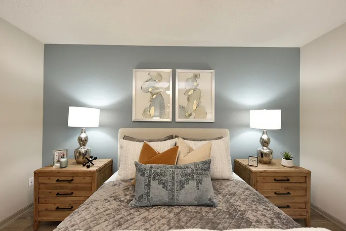 Elegant bedroom with a cozy bed, plush pillows, and soft lighting, featuring modern art and wooden side tables for a warm, inviting atmosphere.