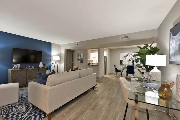 Contemporary living room with elegant blue accent wall, cozy seating area, and stylish open dining space. Features sleek modern furniture and abundant natural light.