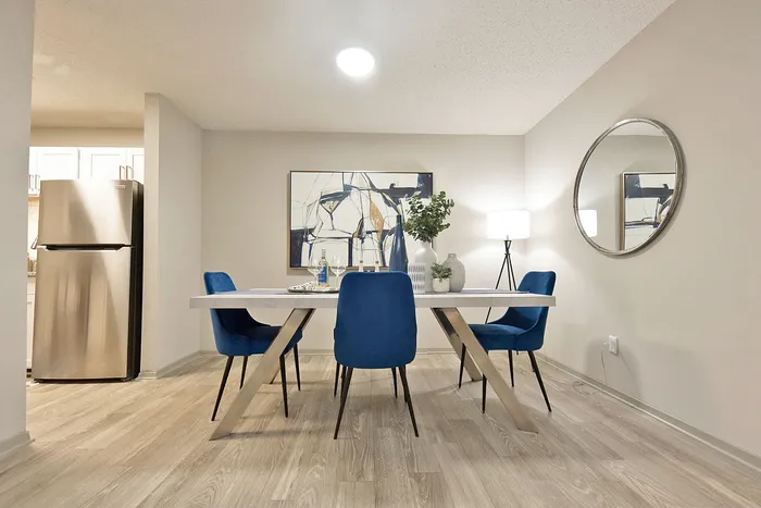Elegant dining area with modern table, vibrant blue chairs, and sleek stainless steel fridge in the background, perfect for stylish entertaining.