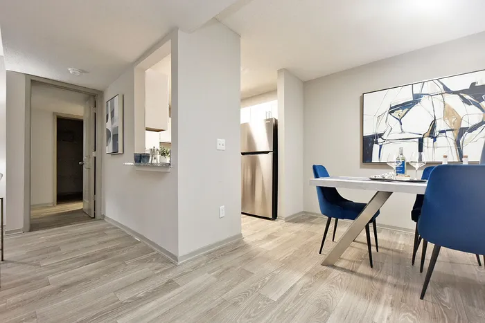 Modern apartment dining area with stylish blue chairs, elegant artwork, and sleek stainless steel appliances.