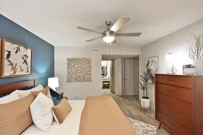 Inviting bedroom with modern decor, featuring a plush, stylish bed, contemporary art, elegant wooden dresser, and soothing blue accent wall.