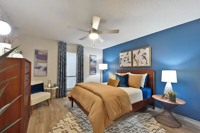Inviting bedroom with modern decor, featuring a cozy bed with gold and blue accents, complemented by elegant wall art and rich wood furnishings.