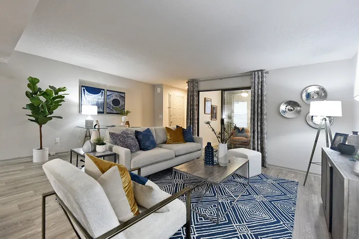 Modern living room with elegant decor, featuring a plush gray sofa and stylish accent chairs. Bright, open space with contemporary art, sleek coffee table, and abundant natural light.