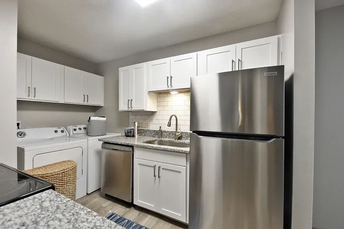 Modern kitchen with stainless steel appliances, sleek white cabinets, and in-unit washer and dryer for convenient living.