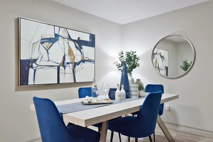 Modern dining room with elegant blue chairs, abstract wall art, and a stylish table setting, perfect for entertaining.