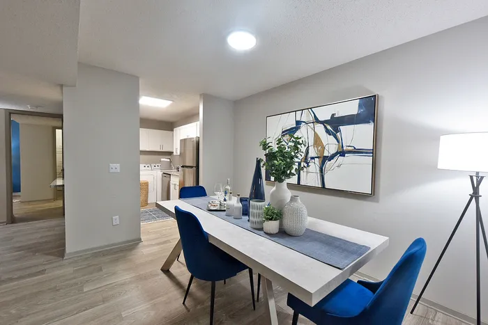 Modern dining area featuring a sleek table with blue chairs, contemporary art, and an inviting kitchen in the background, perfect for entertaining.