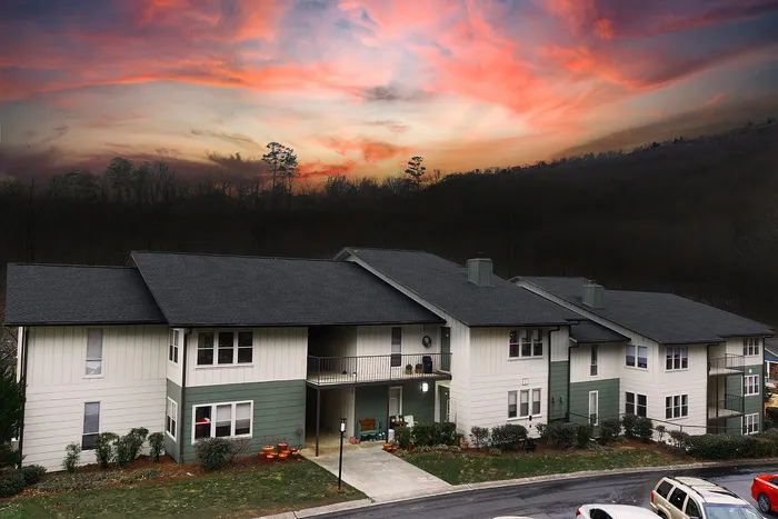 Charming apartment complex under a vibrant sunset sky, featuring modern two-story buildings with balconies and lush greenery.