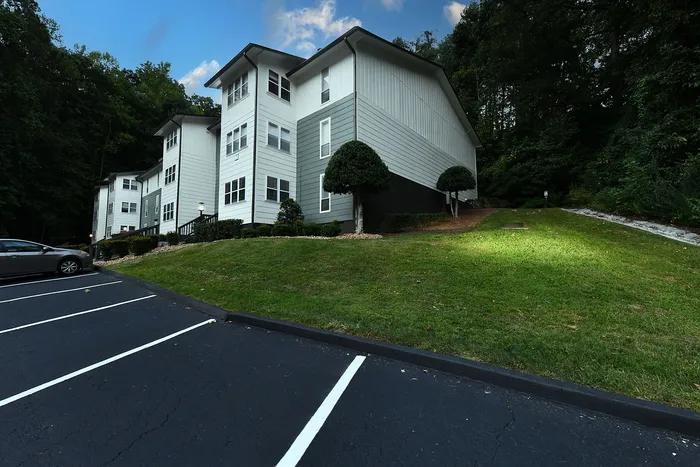 Charming apartment building nestled in a lush green setting, featuring modern architecture and ample parking space.
