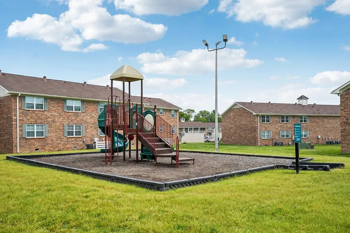 Charming residential community featuring a vibrant playground set against a backdrop of well-maintained brick apartment buildings and lush green lawns.
