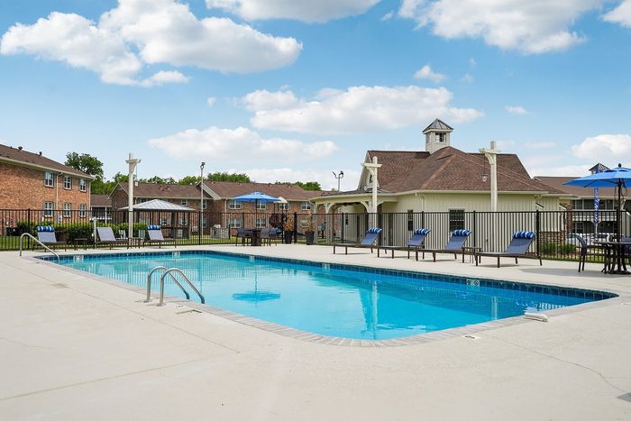 Inviting apartment complex with a sparkling outdoor pool, surrounded by comfortable lounge chairs and vibrant umbrellas, perfect for relaxation and leisure.