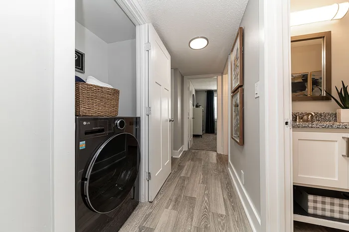 Modern hallway with sleek hardwood flooring, featuring a tucked-away laundry area with an LG washer. Bright and welcoming, leading to a bathroom with stylish granite countertops.