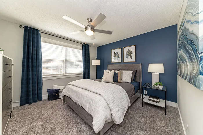 Chic bedroom with plush carpeting, a cozy bed, and elegant decor against a stylish blue accent wall.