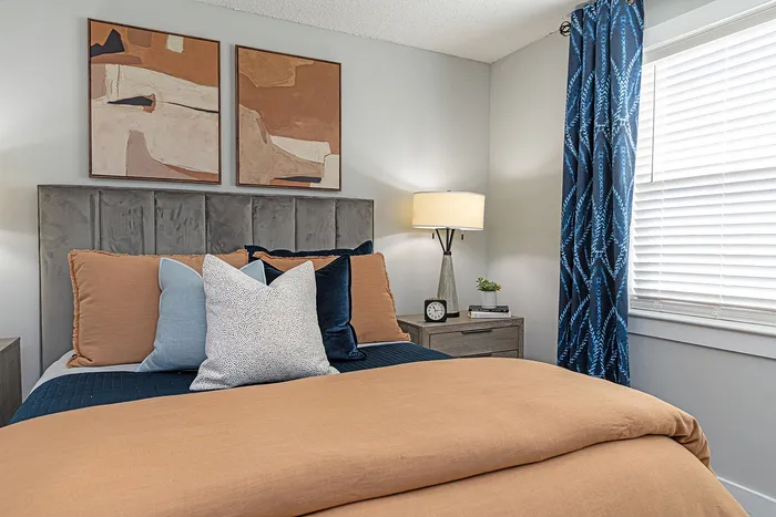 Elegant bedroom with plush orange bedding, stylish abstract artwork, and a cozy ambiance complemented by soft lighting and sophisticated decor.