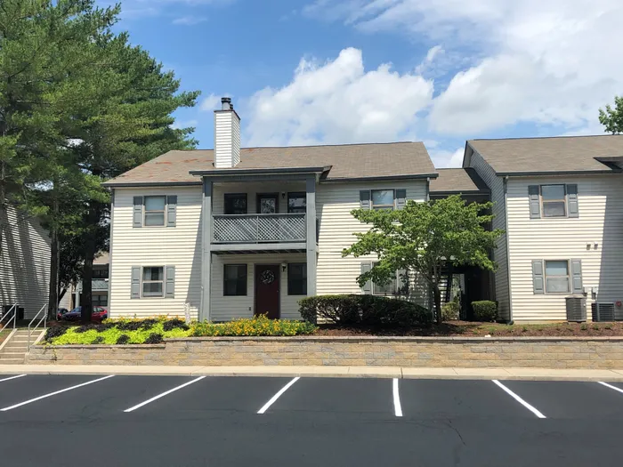 Charming two-story apartment building with a welcoming porch, surrounded by lush greenery and vibrant flower beds, offering an appealing suburban vibe.