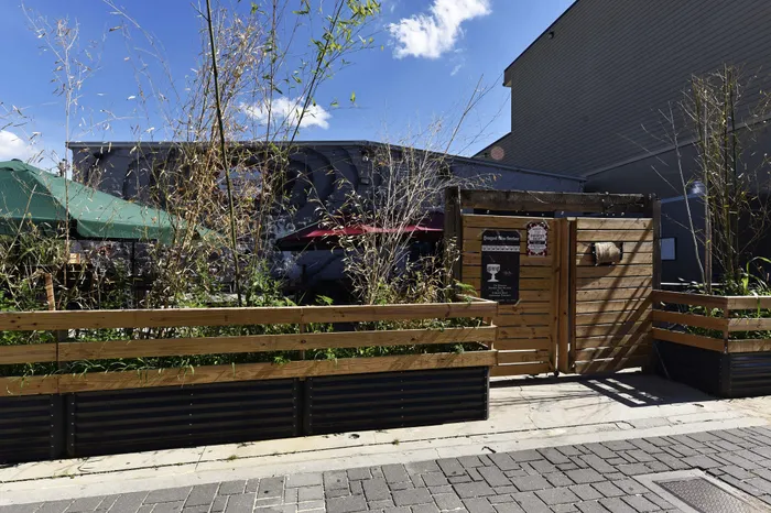 Charming outdoor space with rustic wooden fencing, lush greenery, and vibrant umbrellas against a bright blue sky.
