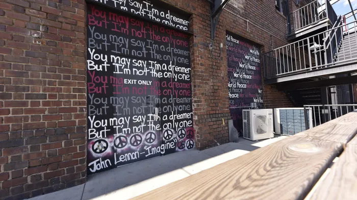 Vibrant wall mural with inspiring peace and dreamer quotes in a modern urban setting, featuring industrial brick and metal staircase architecture.