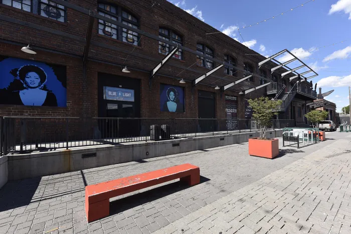 Charming urban streetscape with brick facade and colorful murals, featuring outdoor seating and vibrant planters.