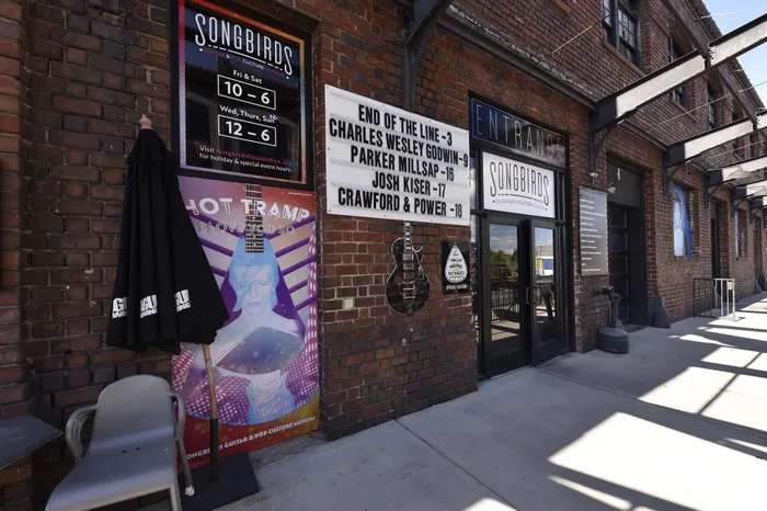Charming entrance to a music venue with vibrant concert posters, set against a rustic brick facade, showcasing upcoming performances at Songbirds Guitar and Pop Culture Museum.