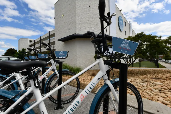 Inviting apartment complex featuring modern white architecture with a convenient bike-share station in the forefront under a vibrant blue sky.