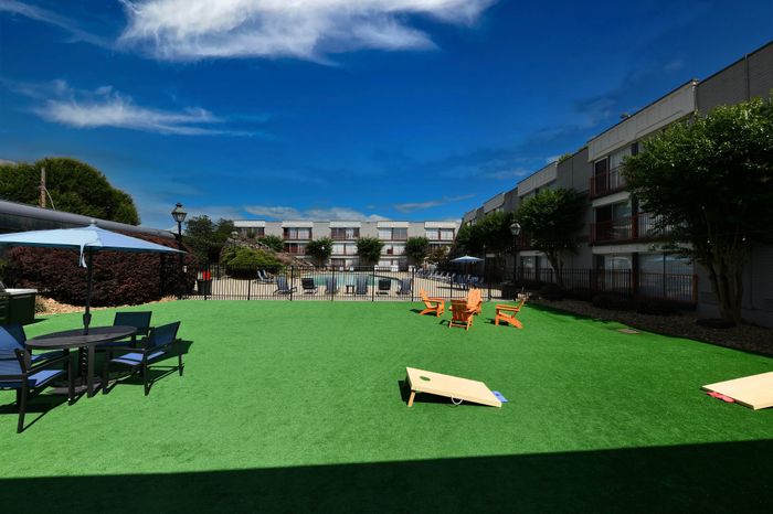 Inviting apartment complex courtyard featuring lush green lawn, cozy patio furniture, and vibrant blue sky backdrop.