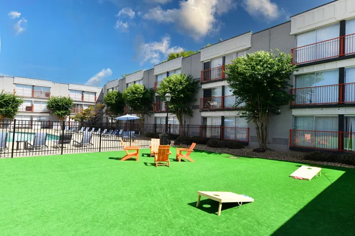 Vibrant apartment complex exterior showcasing lush green courtyard, cozy seating area, and sunlit balconies under a clear blue sky.