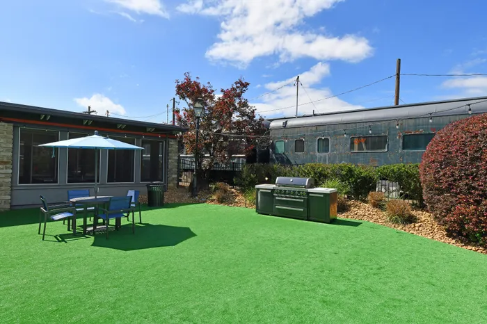 Charming outdoor patio with a barbecue grill, table set with umbrella, and lush green turf, ideal for leisurely gatherings.