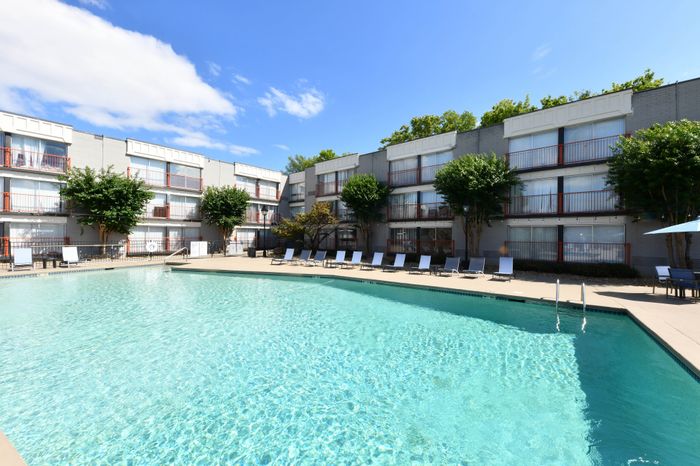 Inviting apartment complex with a sparkling swimming pool, surrounded by modern three-story buildings and lush greenery, perfect for relaxation and leisure.