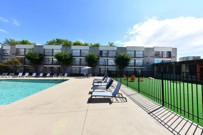 Inviting apartment complex with a sparkling pool, plenty of sun loungers, and lush greenery, perfect for relaxation and leisure.