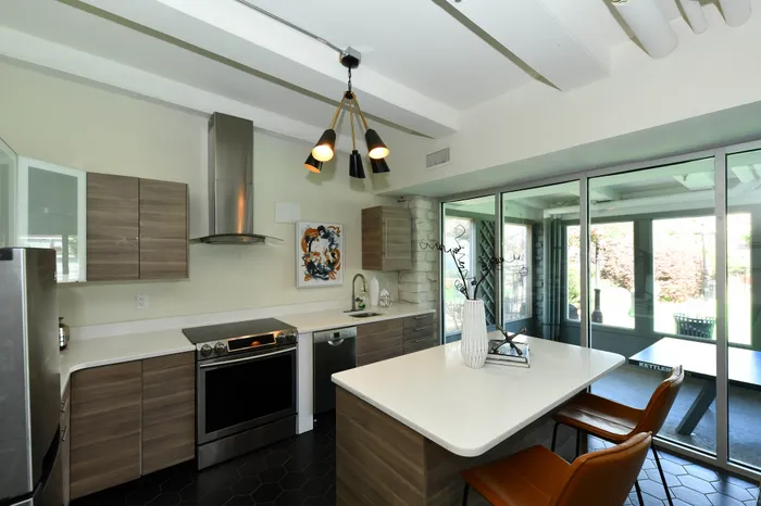 Modern kitchen with sleek appliances, stylish island, and large glass doors opening to a bright outdoor view.