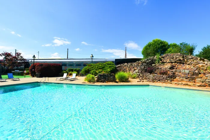 Inviting outdoor pool area with sparkling blue water, surrounded by comfortable lounge chairs and lush greenery, perfect for relaxation and leisure.