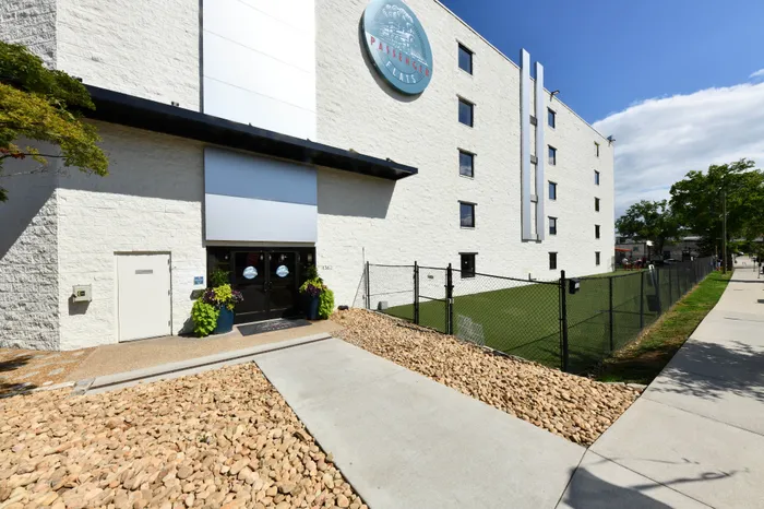 Modern apartment entrance with stylish landscaping, sleek white exterior, and inviting greenery.