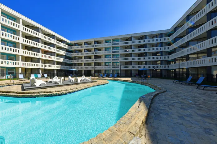 Luxurious apartment complex featuring a sparkling outdoor pool and stylish lounge area under clear blue sky.