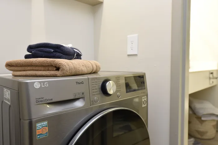 Modern laundry room featuring a sleek LG ThinQ washer, complemented by neatly folded towels on top.