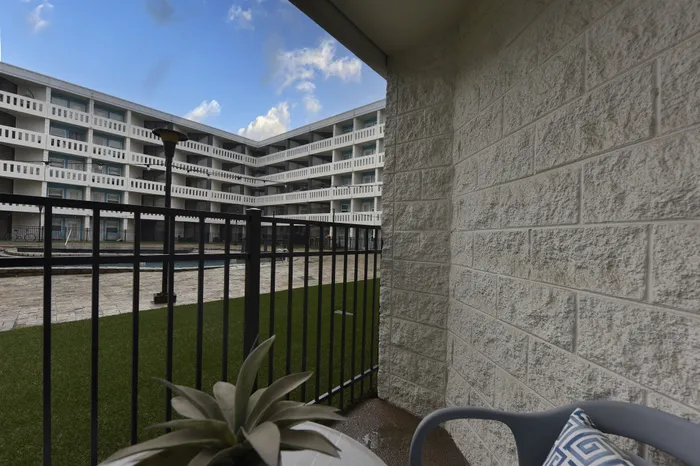 Charming apartment balcony with cozy seating overlooking a modern courtyard and clear blue skies.
