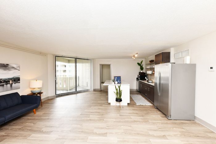 Bright and spacious open-concept living area in a modern apartment, featuring a sleek kitchen with stainless steel appliances and a cozy sitting area with a stylish couch.